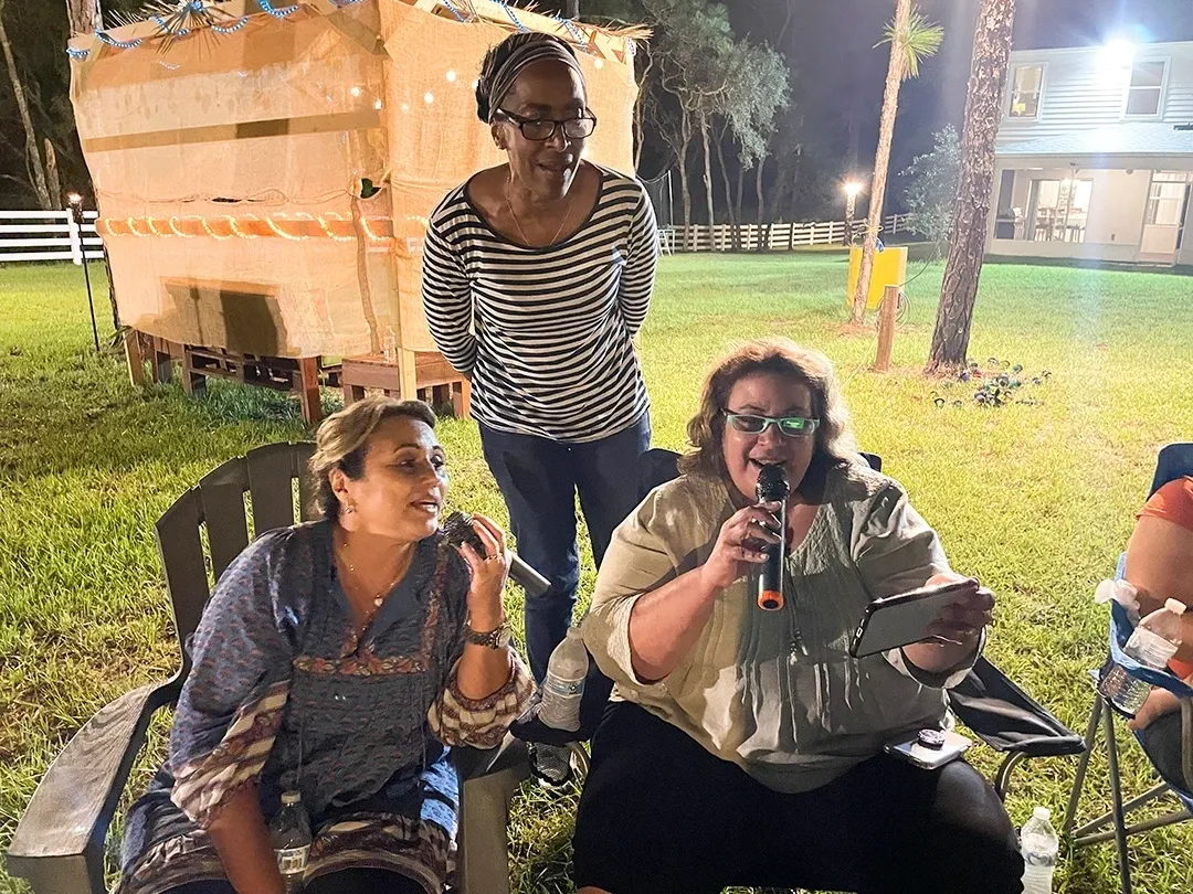 Three women are sitting in a lawn chair and one is singing.
