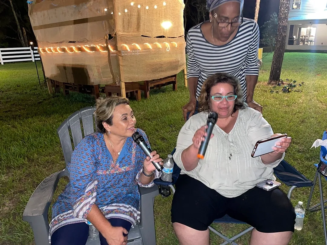 Three women sitting on lawn chairs and one is holding a microphone.
