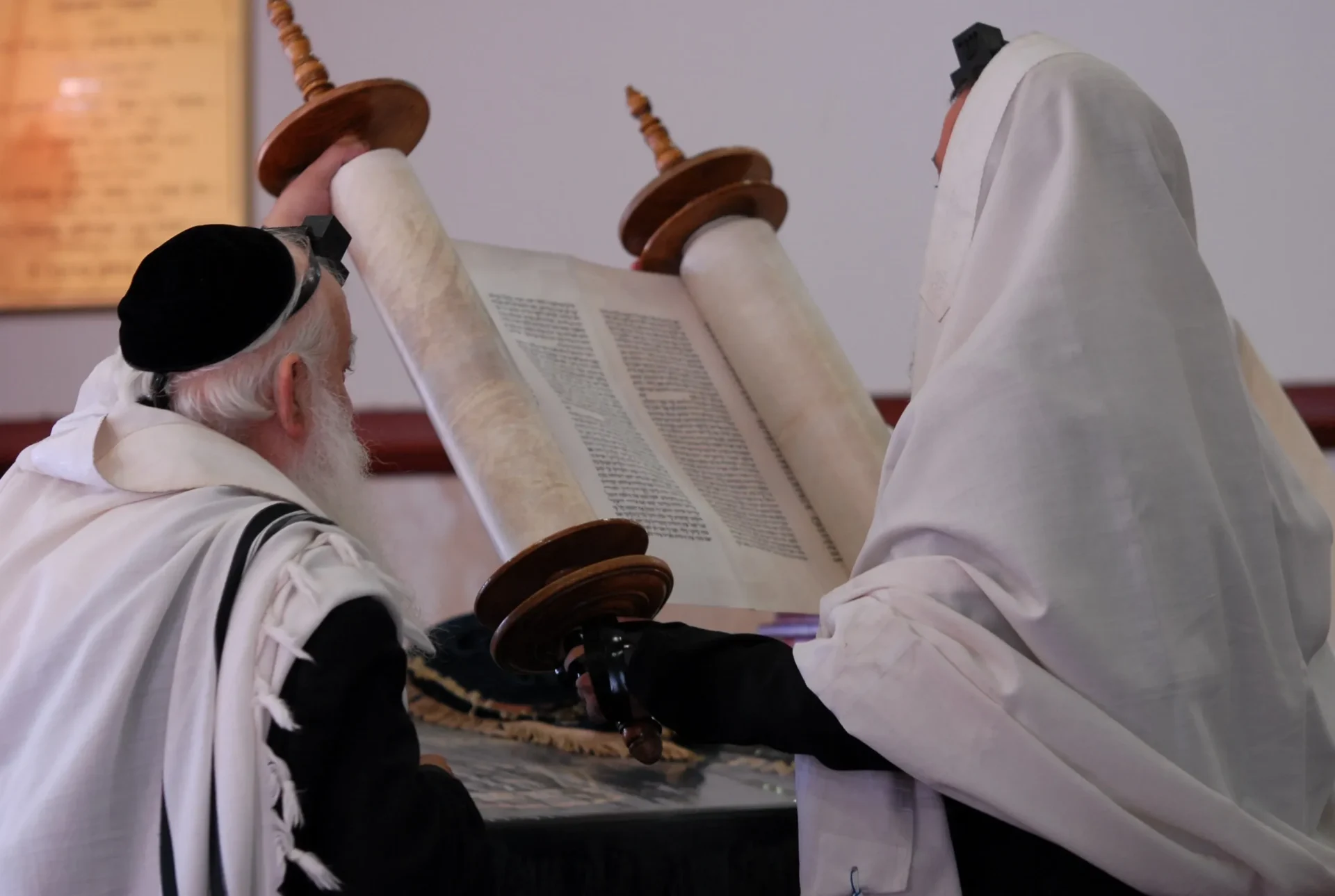 Two men reading a torah scroll in front of a table.