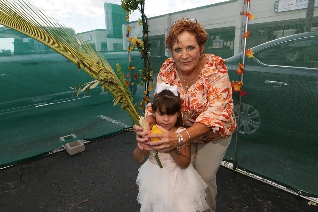 A woman and child holding an orange in front of a car.