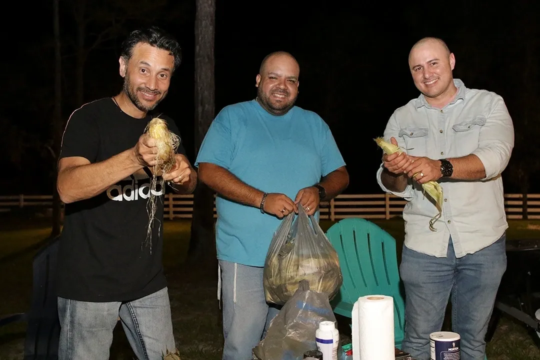 Three men holding bananas and a bag of banana peels.
