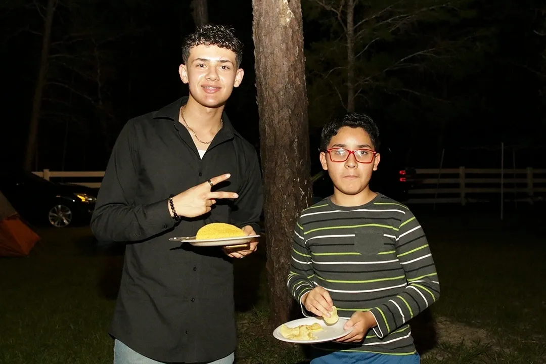 Two young men holding plates of food in front of a tree.