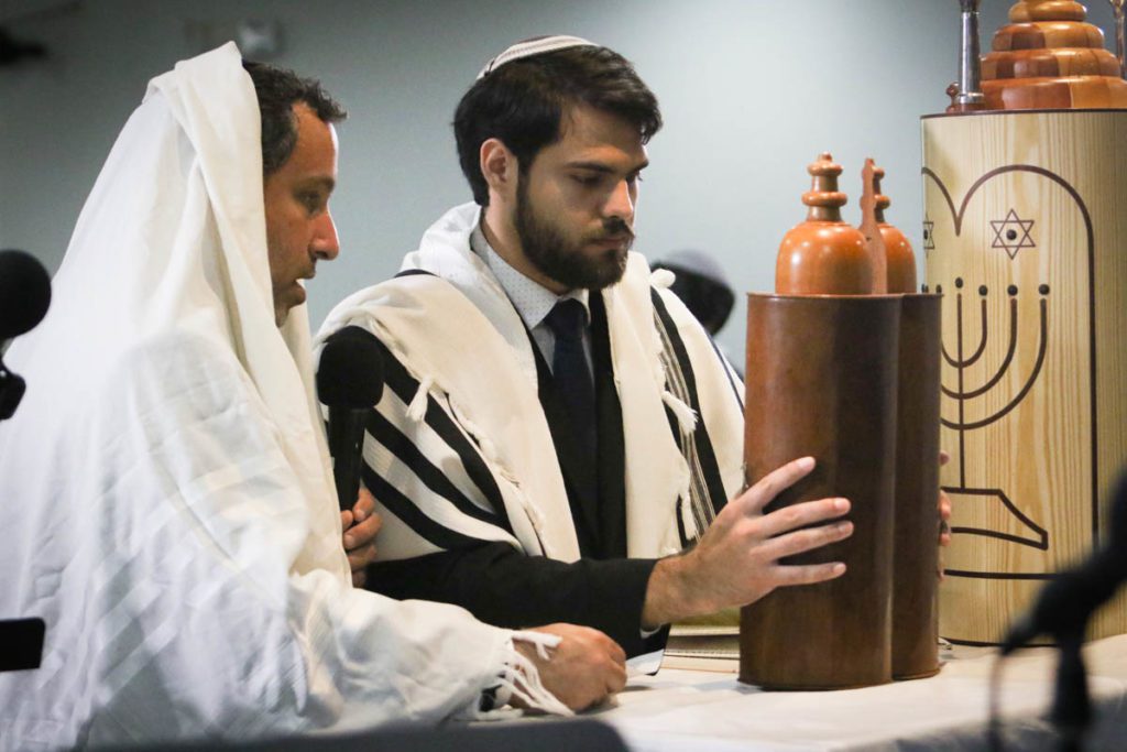 Two men in traditional jewish clothing are looking at a torah.