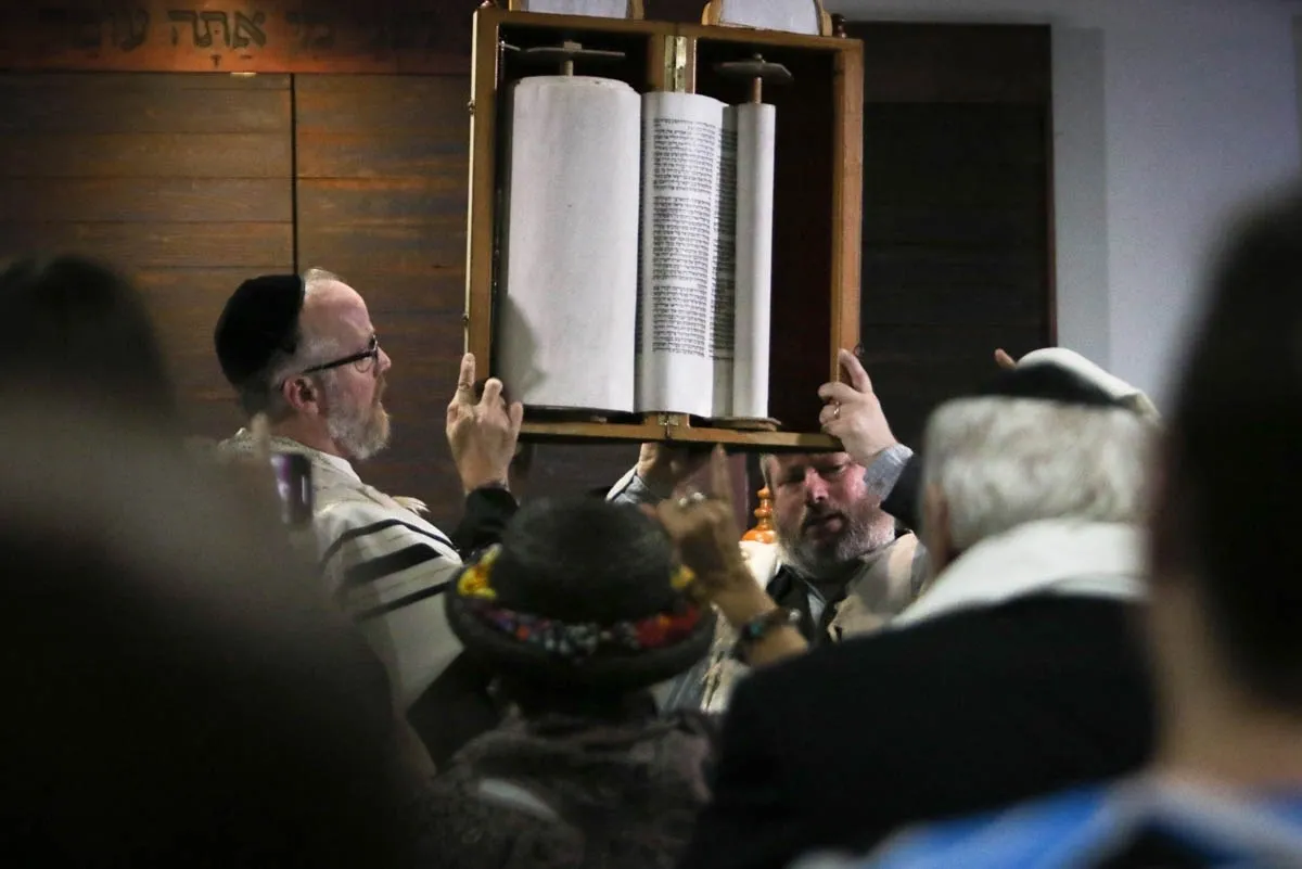 A man holding up a torah scroll in front of people.