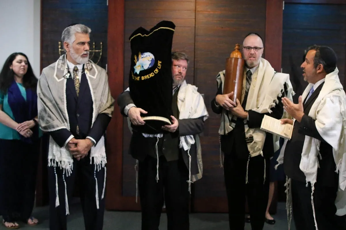 A group of people standing around each other holding up a torah.