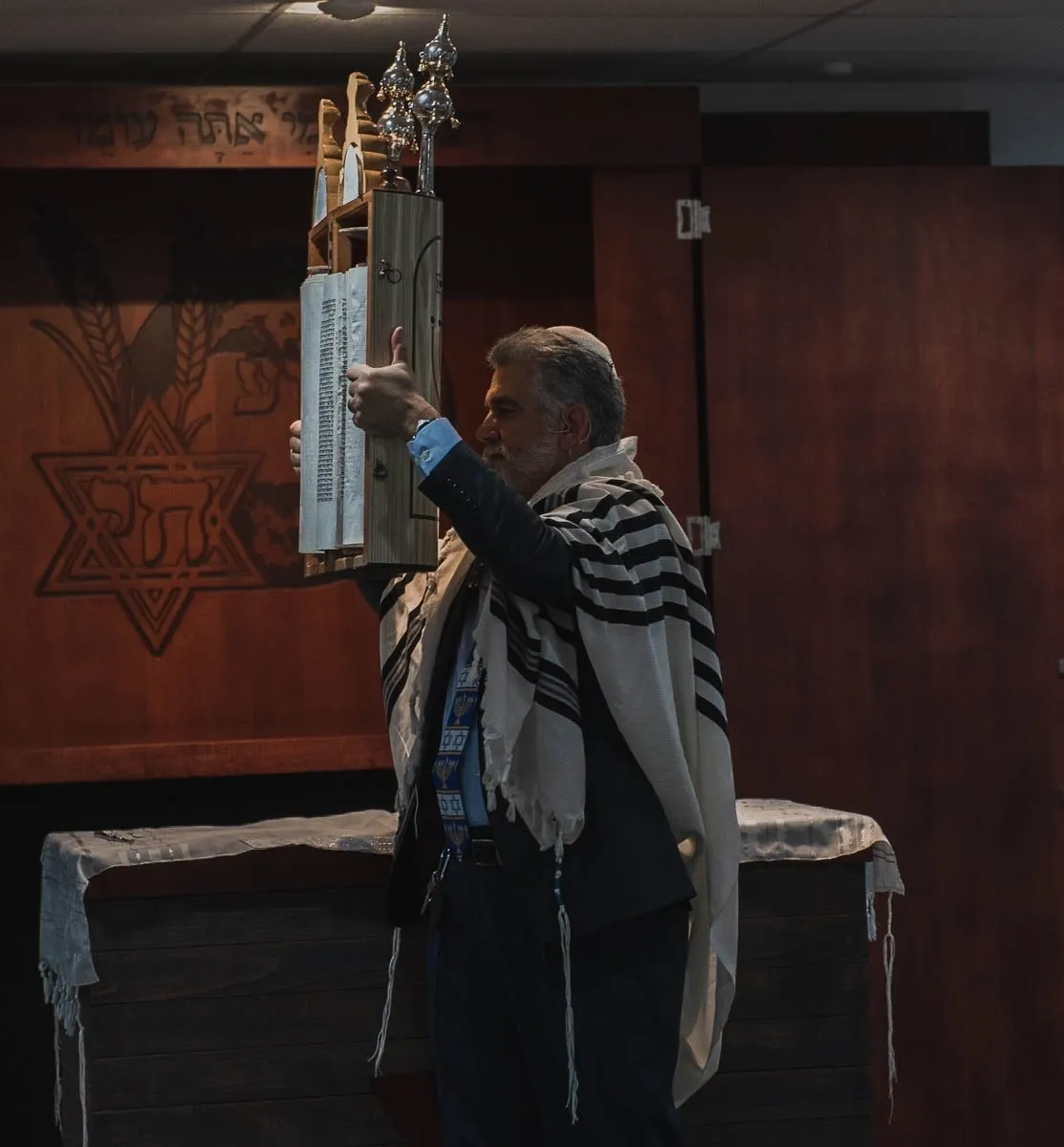 A man in a synagogue holding up a torah.