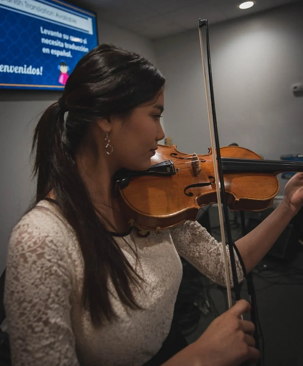 A woman playing the violin in front of a television.
